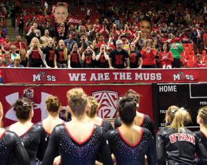The Utah gymnastics team stands in front of fans who are standing behind a “We Are the MUSS” banner.
